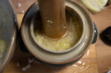 Load image into Gallery viewer, A close-up of a handmade ceramic fermentation crock, with a wooden pickle packer pounding sauerkraut
