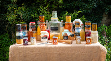 Load image into Gallery viewer, Assorted fermented food jars and bottles on a table outdoors with greenery in the background
